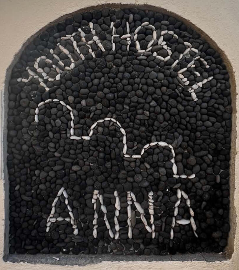 Youth Hostel Anna pebble sign under a Cycladic arch in Perissa, Santorini
